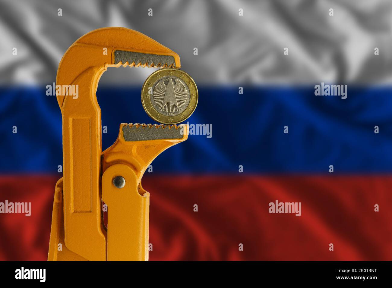 One euro coin clamped in an orange plumber wrench on the background of the Russian flag. Obverse side Stock Photo