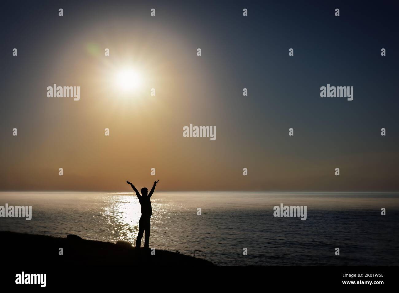 A woman performs her morning yoga poses as the sun rises on Lake Michigan at the Mariners Trail in Manitowoc, Wisconsin. Stock Photo
