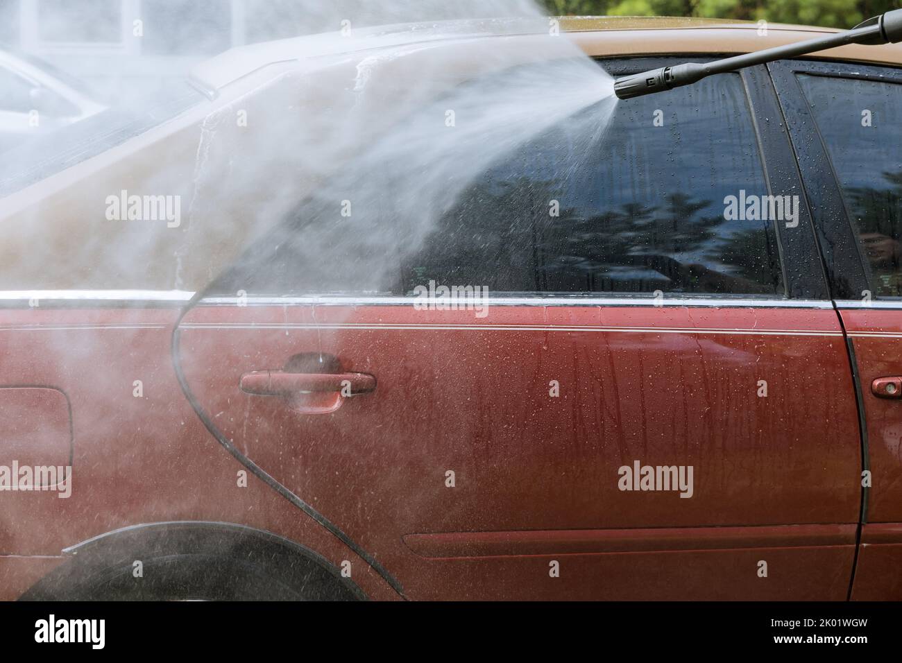 During the process of washing his car, a worker sprays high-pressure jets of water onto his car while simultaneously cleaning it Stock Photo