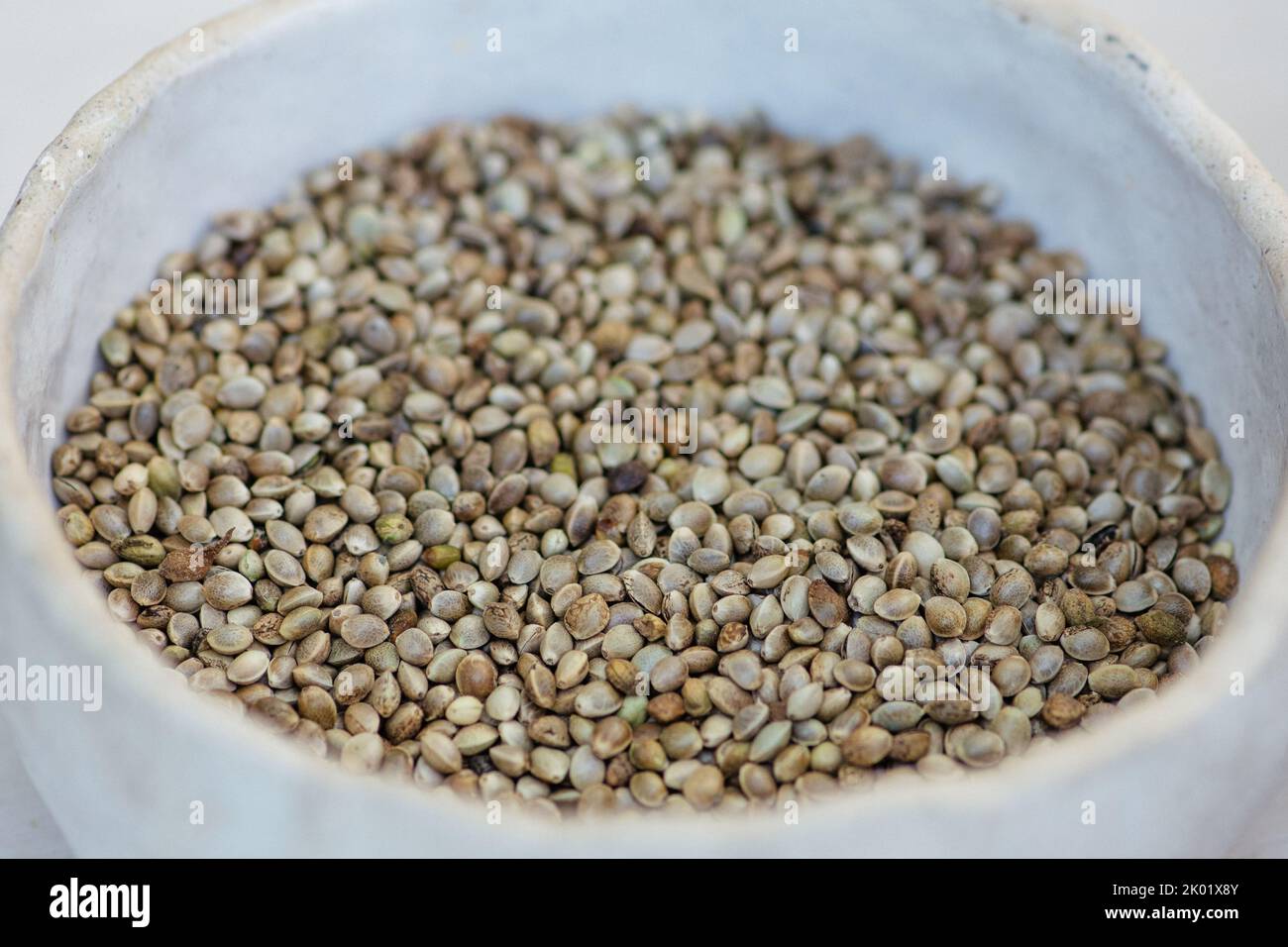 Dried hemp cannabis seeds in a white ceramic bowl, close up Stock Photo