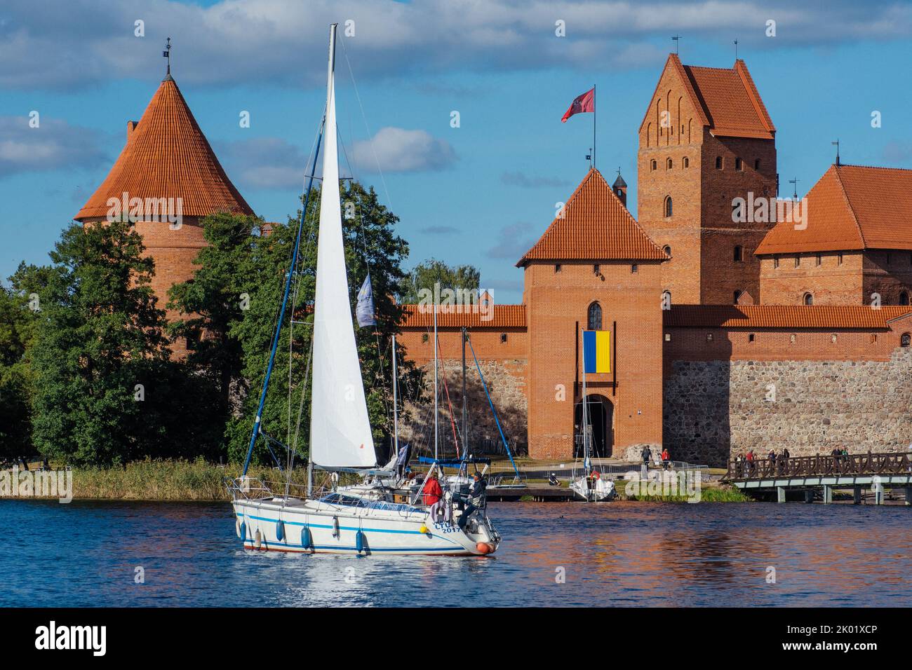 Medieval castle of Trakai, Vilnius, Lithuania, Europe, surrounded by beautiful lakes and nature with wooden bridge, sail boat and Ukrainian flag Stock Photo