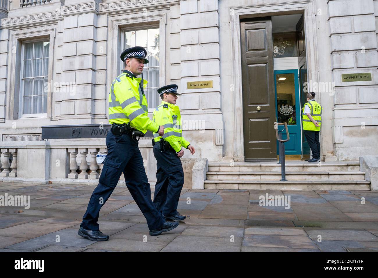 Police officers patrolling past the UK government Cabinet Office, 70 Whitehall, Westminster, London, UK. Security on door Stock Photo