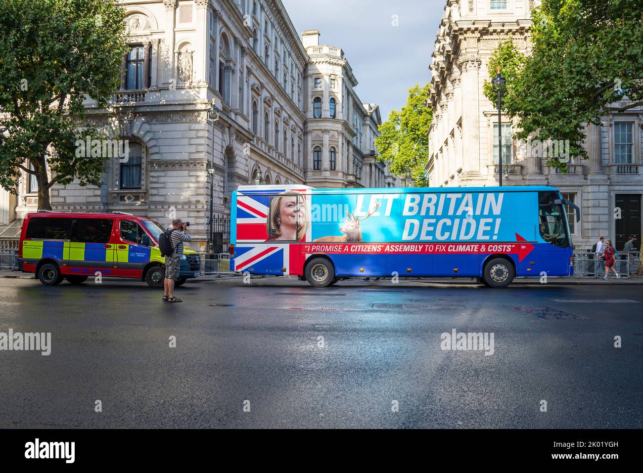A hoax bus from Extinction Rebellion with the appearance of a Liz Truss campaign bus, outside Downing Street. Citizen's assembly slogan. Police van Stock Photo