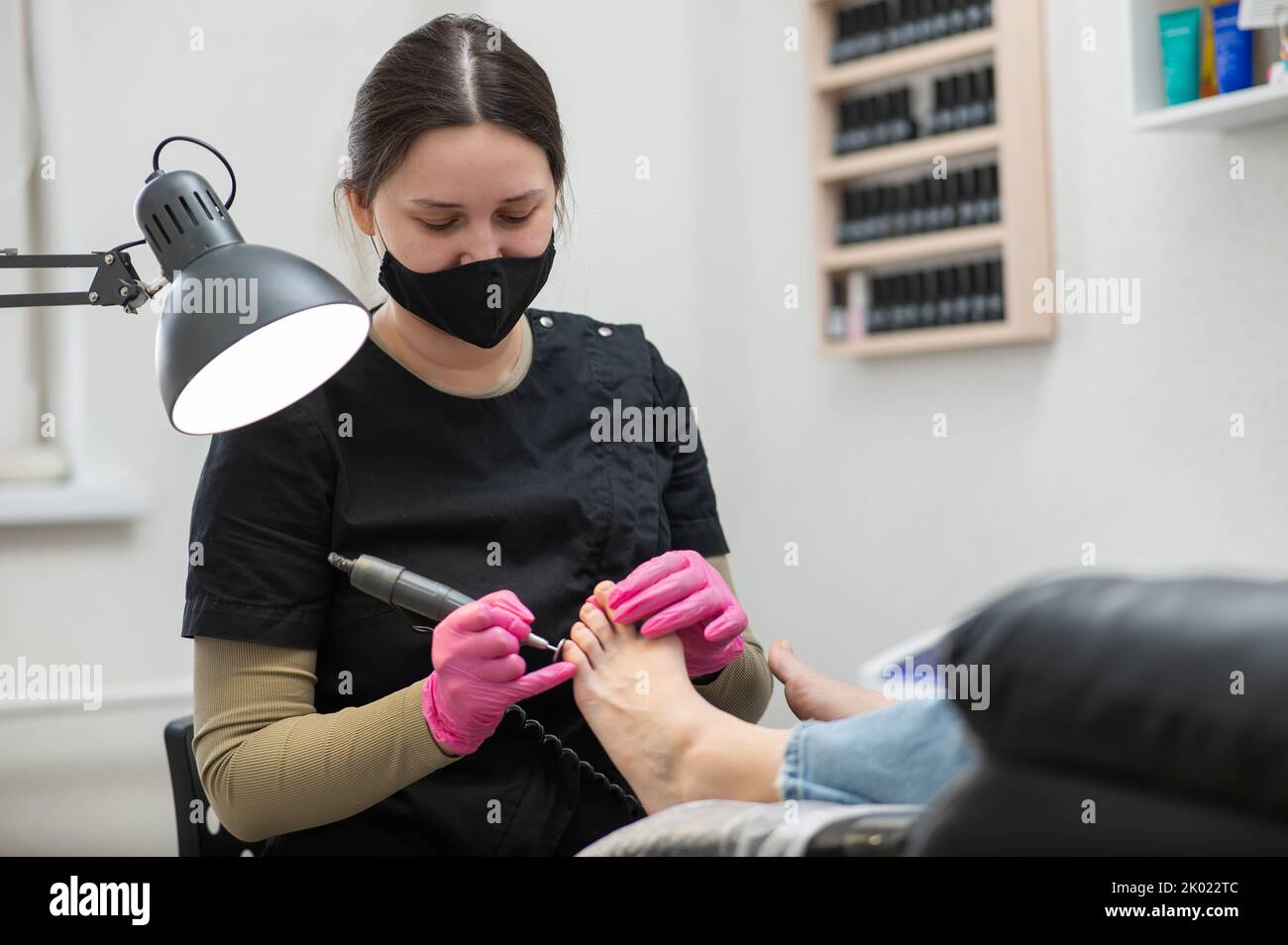 The pedicure master processes the client's foot using an apparatus with an abrasive disc. Stock Photo