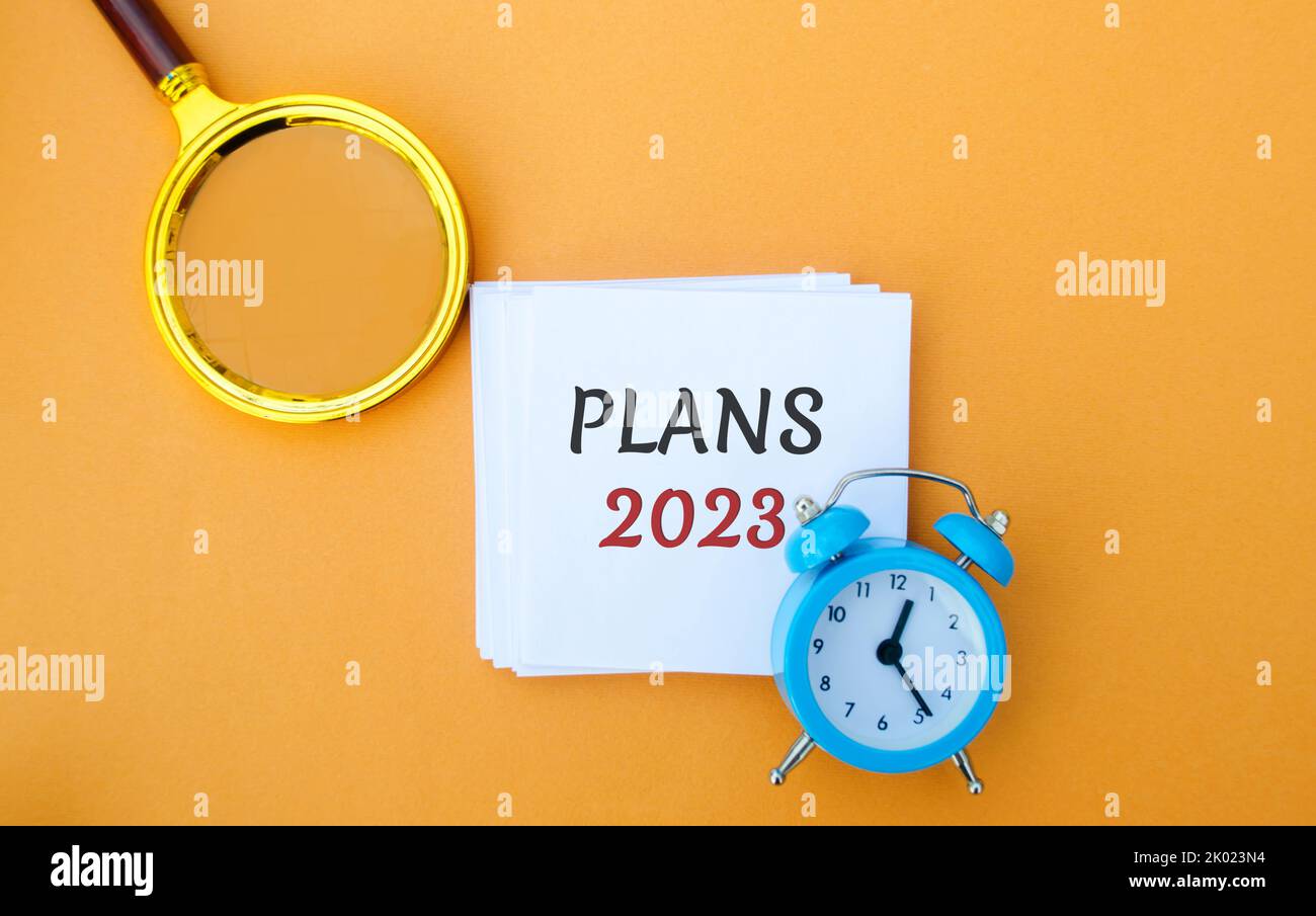 Note with words Plans 2023. Setting goals and planning targets for the next year. Motivation, vision. Business and finance concept. Magnifying glass a Stock Photo