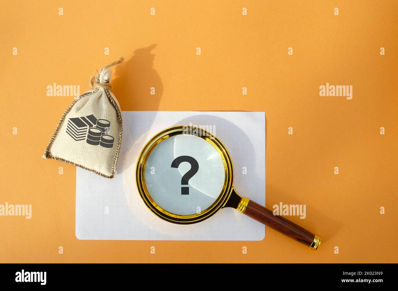 Magnifying glass with a question mark and a money bag. Business and finance concept. The question of investment. Financial problems and difficulties. Stock Photo