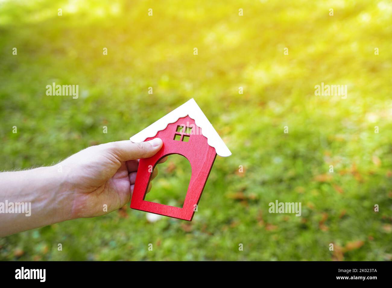 Miniature wooden house in the hands of a man outdoors. Real estate concept. Eco-friendly home. Buying a housing outside the city. Red roof. Selective Stock Photo