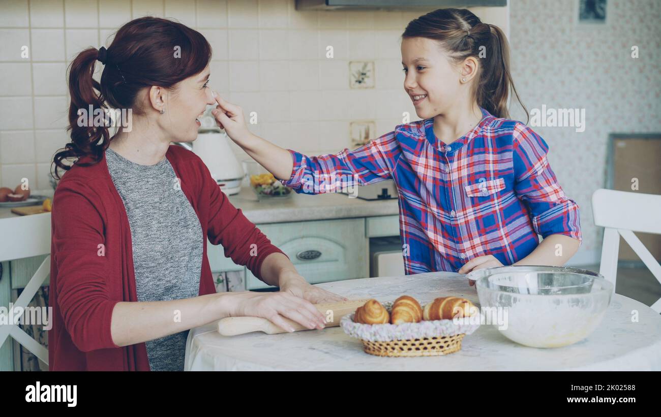 Young mother and her cute daughter have fun smearing nose each other with flour while cooking together in the kitchen on holidays. Family, food, home and people concept Stock Photo