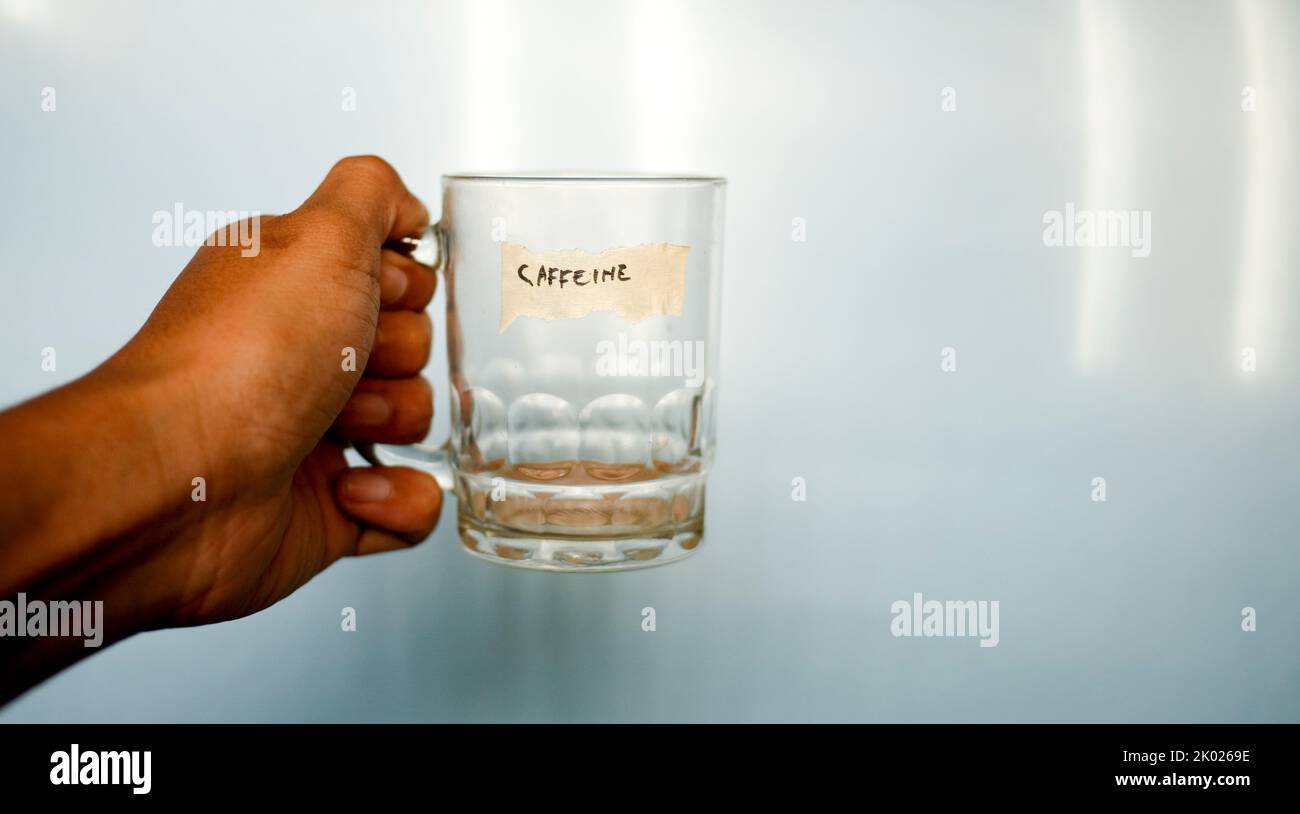 close up hand holding empty drinking glass with text word caffeine