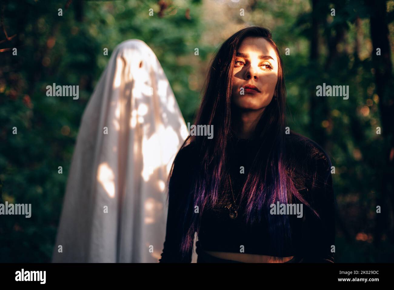 Ghost standing behind young woman in forest during Halloween Stock Photo