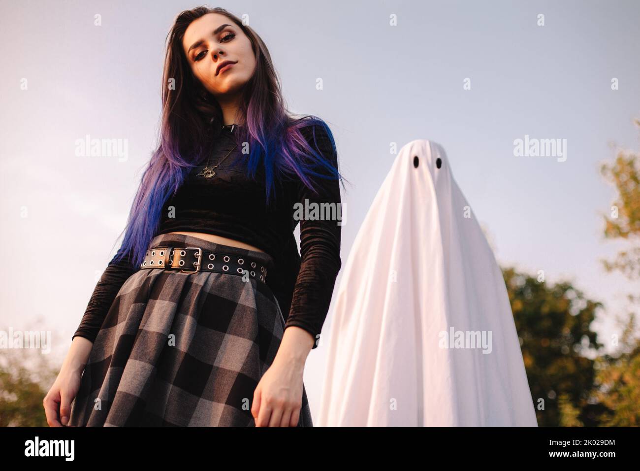 Young woman standing with ghost against blue sky outdoors during Halloween Stock Photo