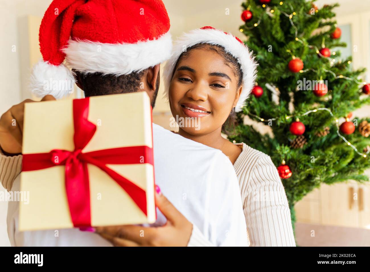 afro american couple giving gift box to each other in house near