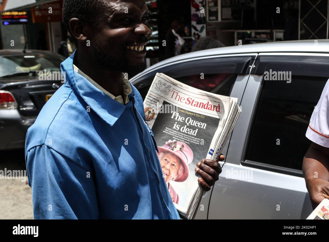 A newspaper vendor is seen smiling while holding newspapers with a front page image of Queen Elizabeth II. Queen Elizabeth II died on Thursday, September 8, 2022, at the age of 96. Stock Photo
