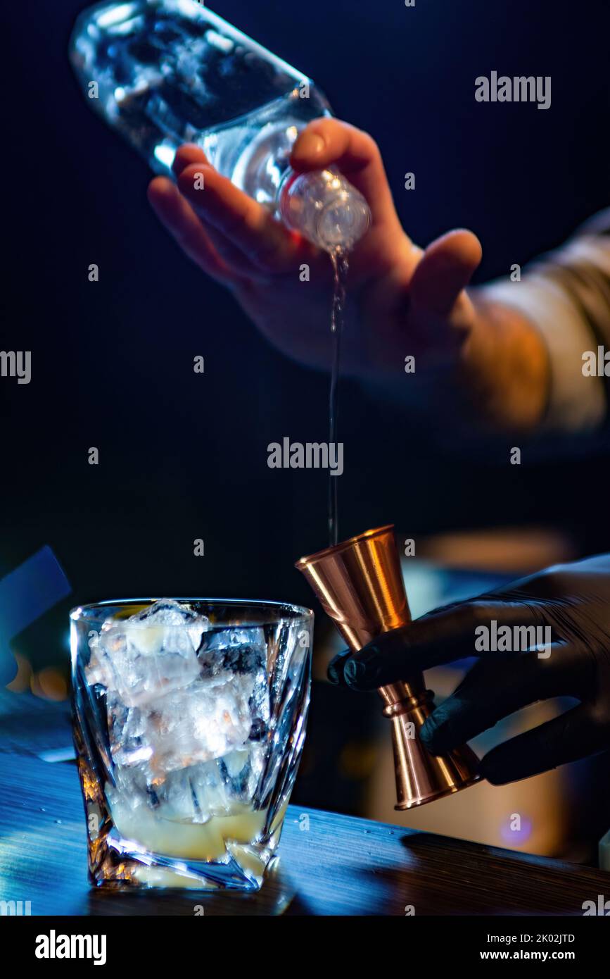 The bartender pours alcohol into a jigger. Bartender is preparing a