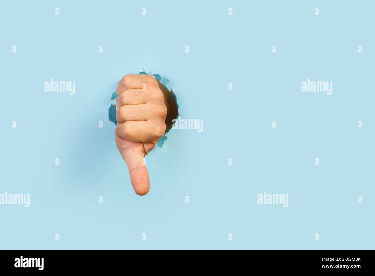 Man hand with thumb down gesture through a hole in a light blue ...
