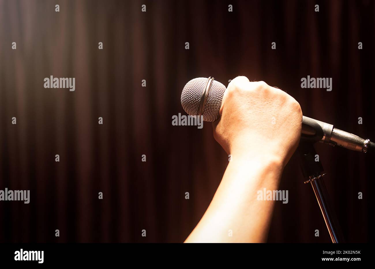 Men's hand holding a microphone Red curtains as a background with copy space Stock Photo