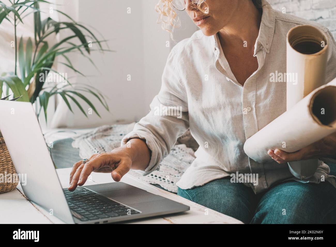 Designer at work in home office using laptop. Woman using laptop and wireless technology. Modern people with computer and paper working online. Indoor leisure activity people and connection business Stock Photo