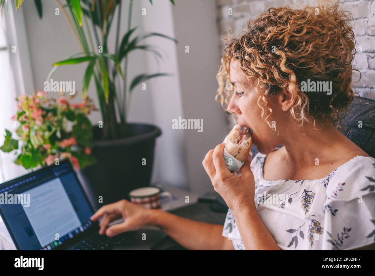 One woman working on laptop and eating a sandwich for lunch break time. Modern people work on computer at home. Alternative office and digital online job concept. Fast food nutrition concept lifestyle Stock Photo