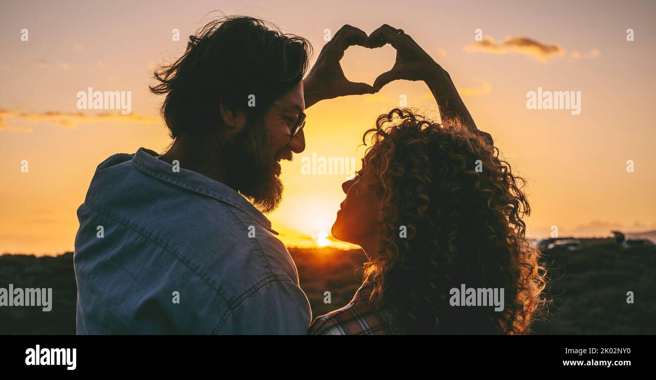 Peace and love with couple doing heart gesture sign with both hands together. Sunset light and outdoor romantic activity with adult man and woman enjoying relationship. Stop war concept Stock Photo