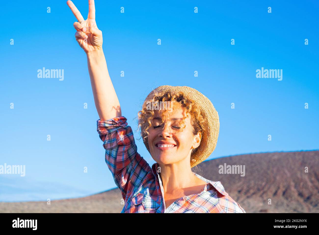 Victory hand gesture to stop war and love peace for people concept image with happy adult woman in the country side, smiling and enjoying the day. Environment and good future for earth supporter Stock Photo