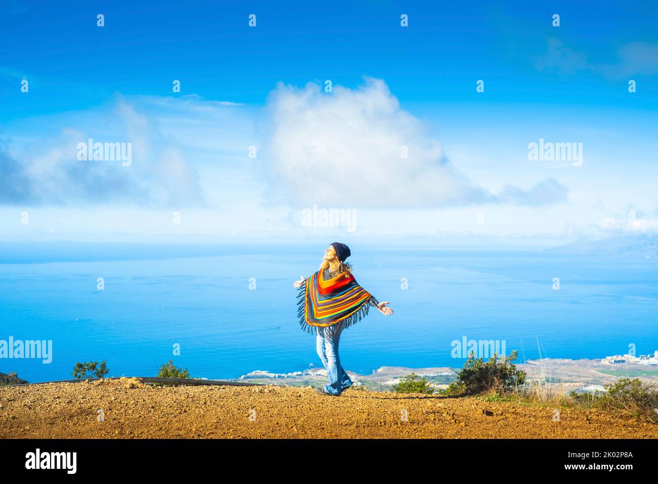 Overjoyed woman tourist opening and outstretching arms in front of a blue sea and sky scenic beautiful background. Happy travel lifestyle for female people wearing colorful clothes Stock Photo