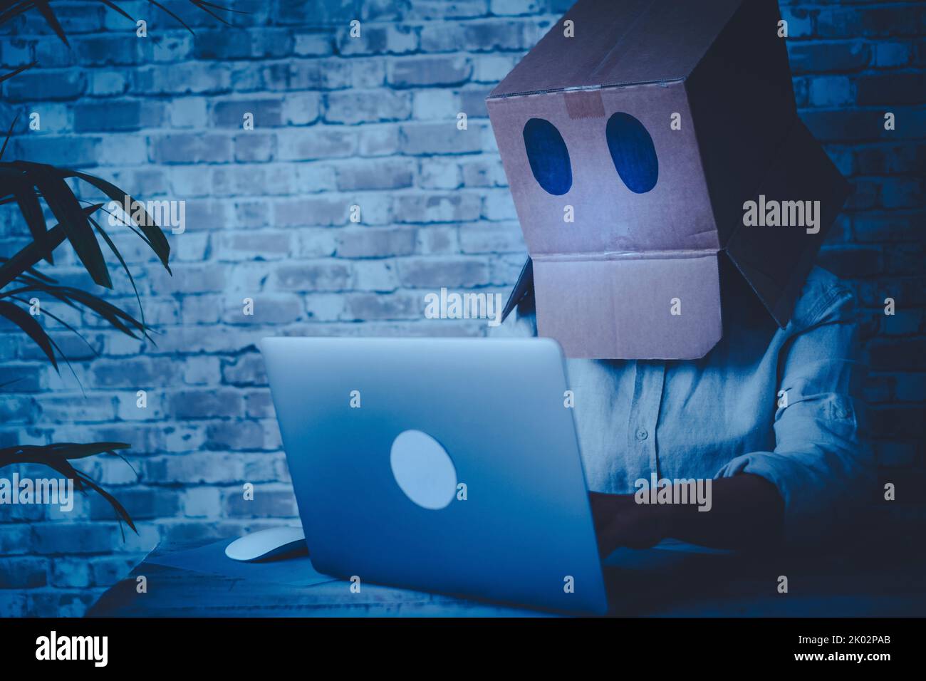 Anonymous hacker use laptop computer and connection at home wearing a box on his head to be not