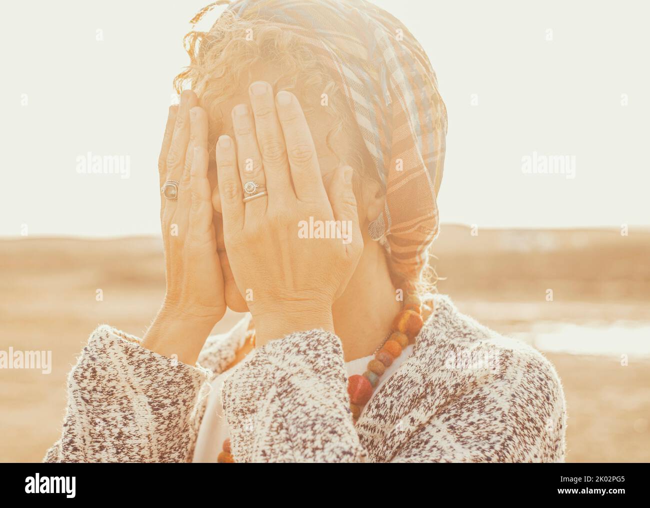 Close up portrait of female people hidden her eyes with hands to don't see around. Concept of surprise or scared woman. Worried about future woman in sunset atmosphere light and outdoors park Stock Photo