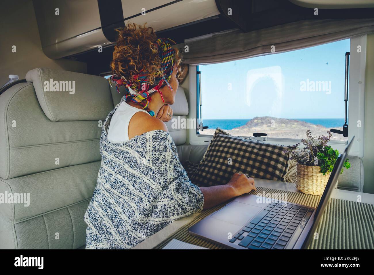 People in work and travel online modern activity business lifestyle. Woman looking outside from camper van interior sitting at the table with laptop computer. Concept of digital nomad life Stock Photo