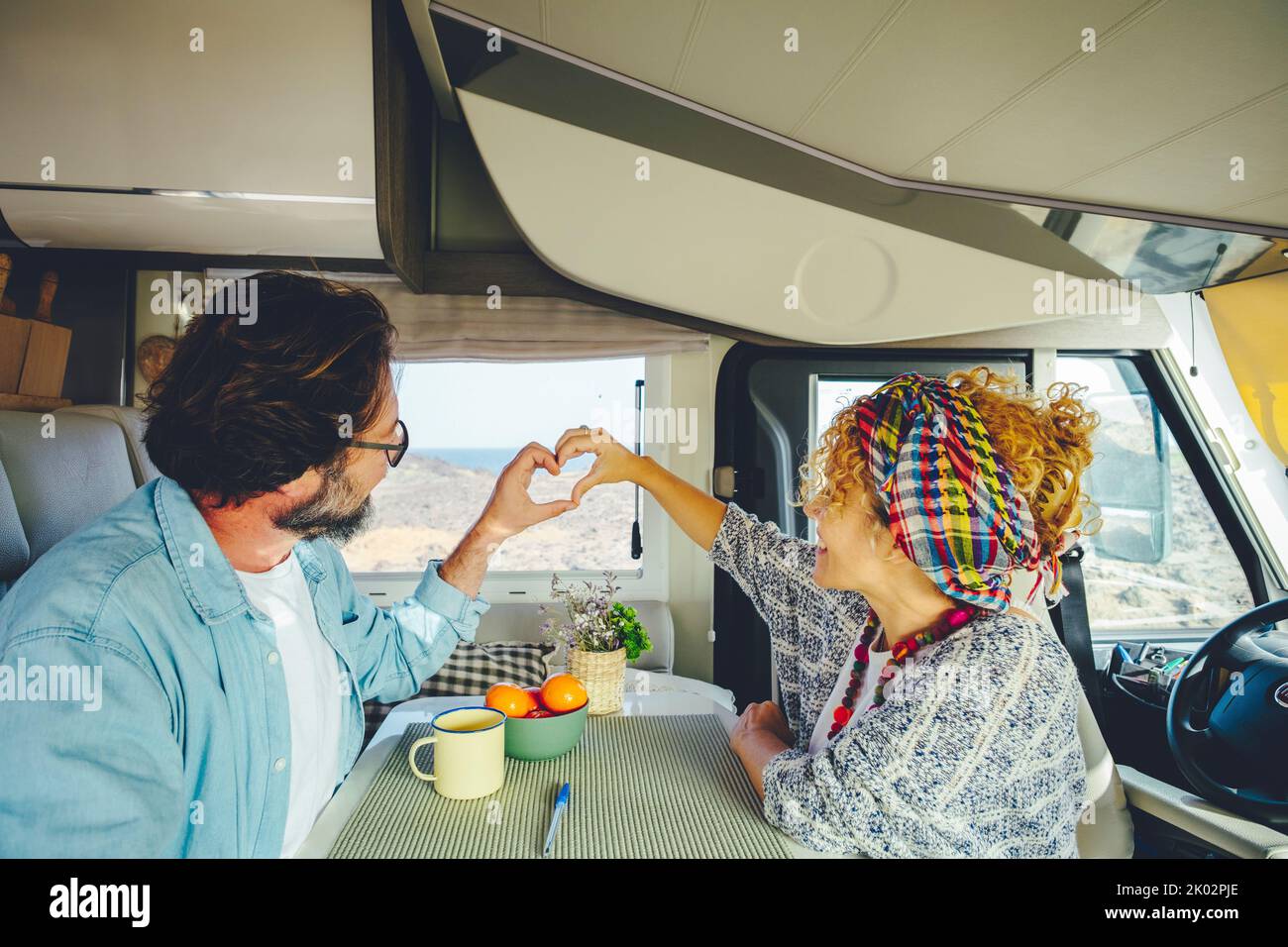 Happy mature couple doing heart gesture sign with hands together inside modern camper van vehicle. Concept of traveler and road trip holiday vacation lifestyle. Man and woman Stock Photo