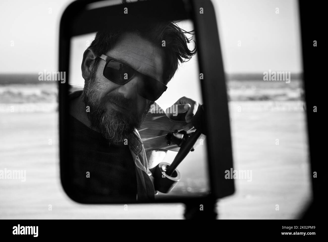 Black and white handsome man portrait in car vehicle mirror. Concept of adventure lifestyle and fashion beard style people. Adult mature model with sunglasses Stock Photo