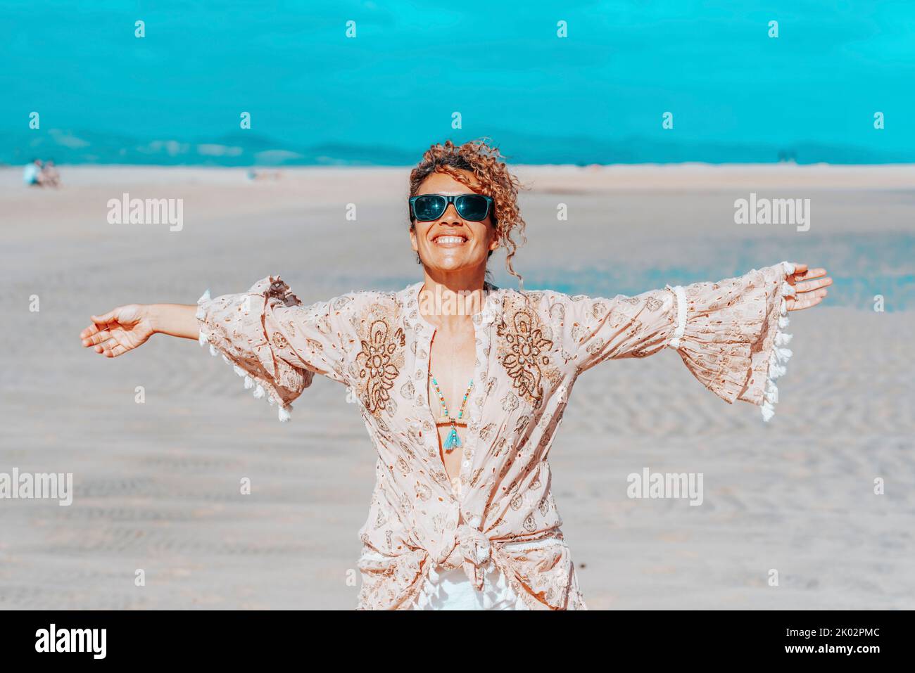 Happy standing pretty adult woman at the beach outstretching arms with tropical summer holiday beach and ocean in background. Concept o travel and wanderlust active female solo people lifestyle Stock Photo