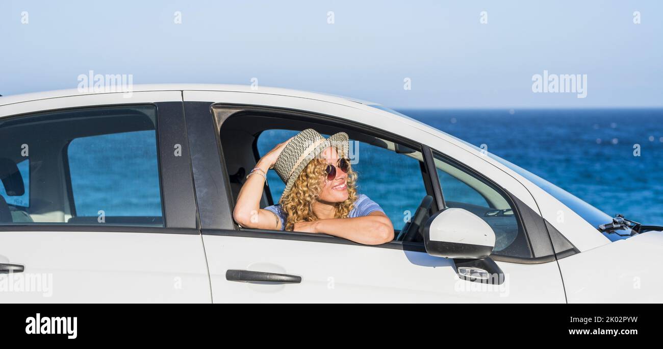 Cheerful happy young woman smile and enjoy travel with car. Blue ocean and sky in background. Female people sitting and admiring outside the vehicle window. People and transport. Summer vacation Stock Photo