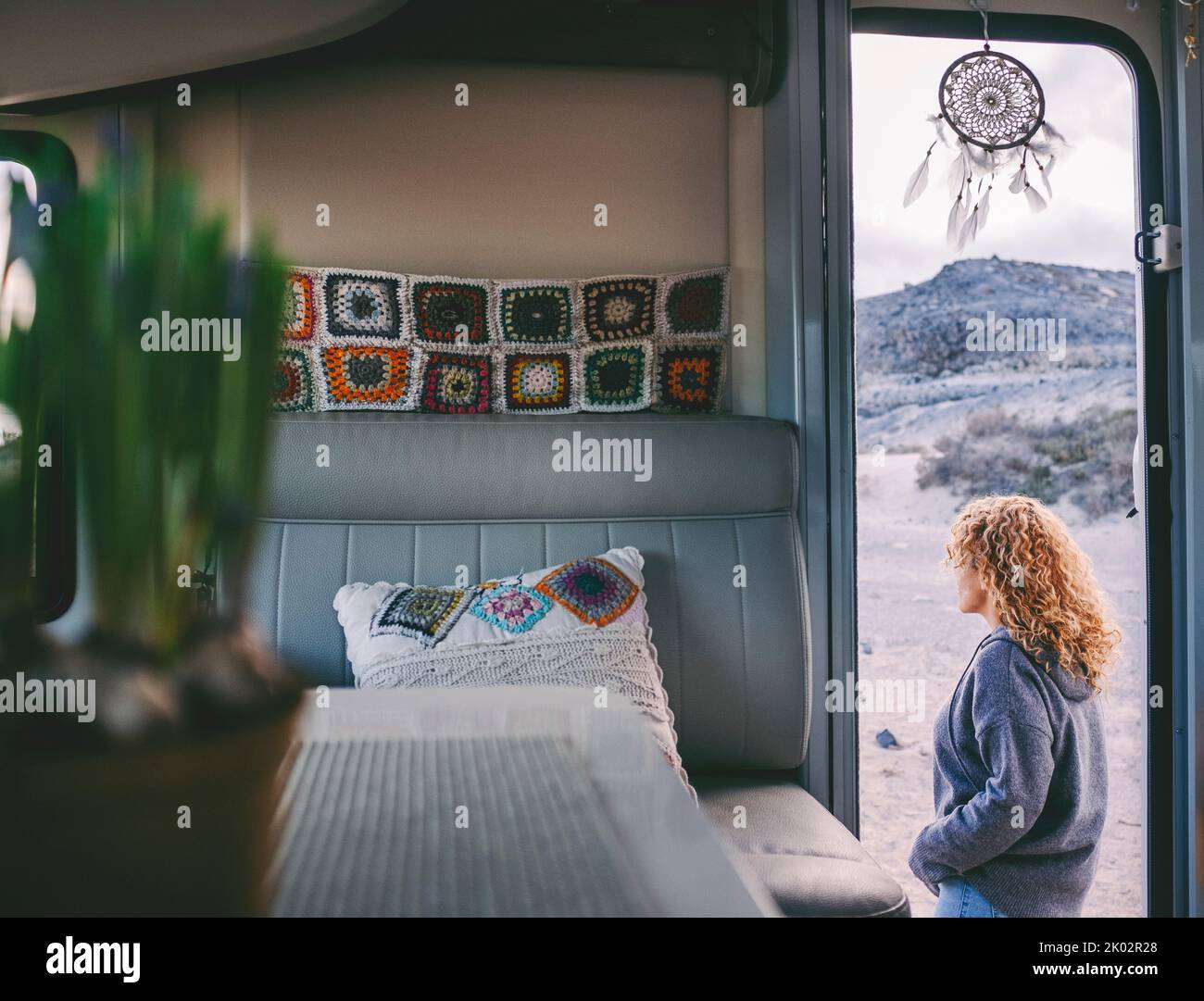 Woman walking outside her camper van. View from interior. Knit decorations inside. Concept of travel and rv motorhome vanlife lifestyle with traveler female people enjoying outdoors Stock Photo