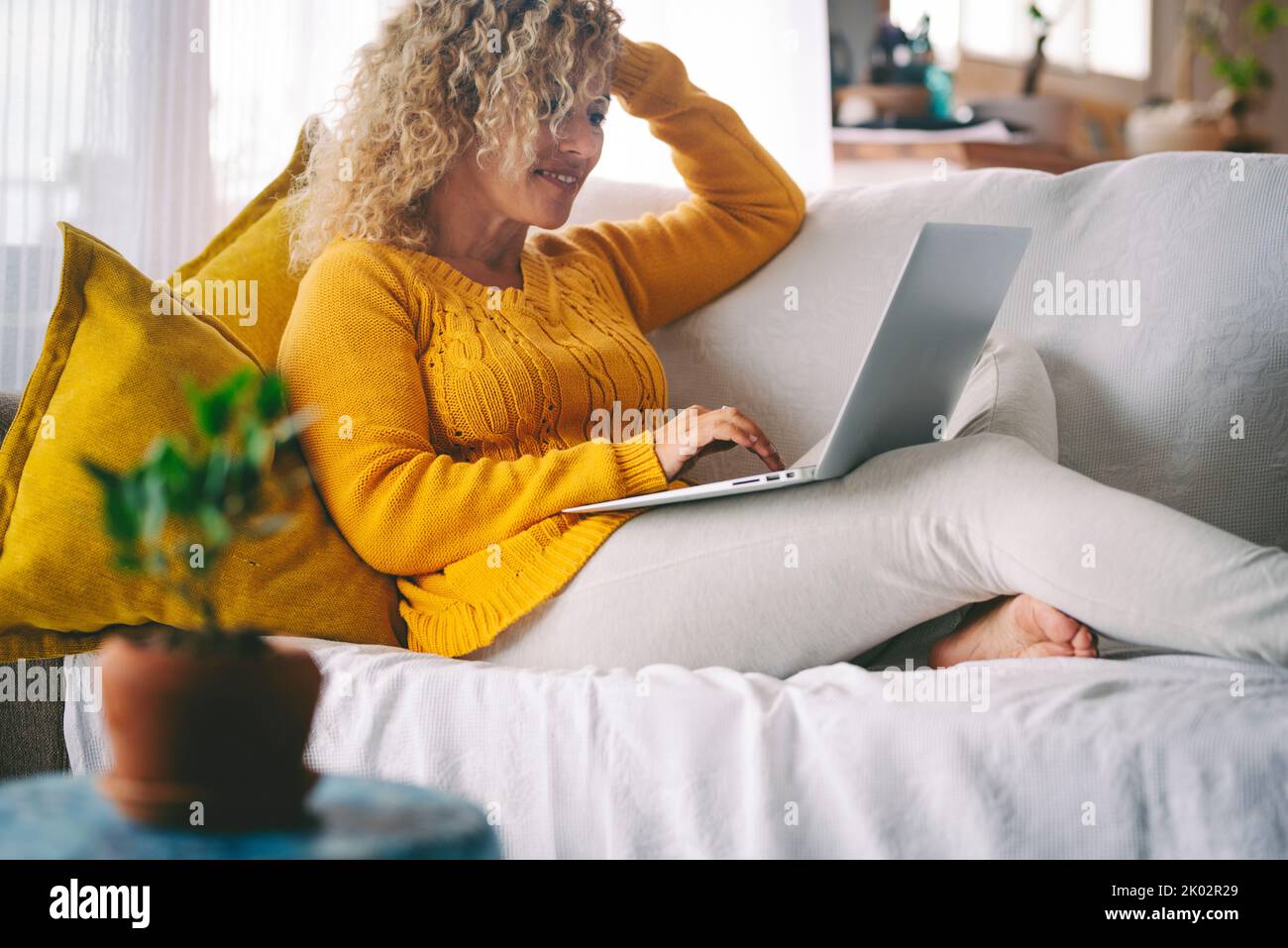 Adult woman in indoor home technology leisure activity using laptop computer to surf the web and smile. Online job business work. Happy female people in video call connection Stock Photo