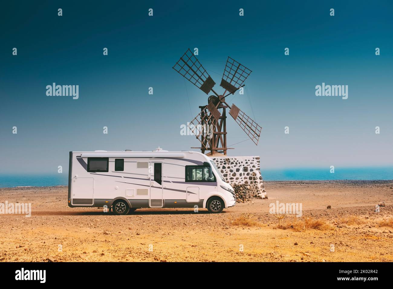 Big modern camper van motorhome parked near an old windmille in the desert. Concept of wild and free campsite and off grid life. Travel people and alternative home on wheels Stock Photo