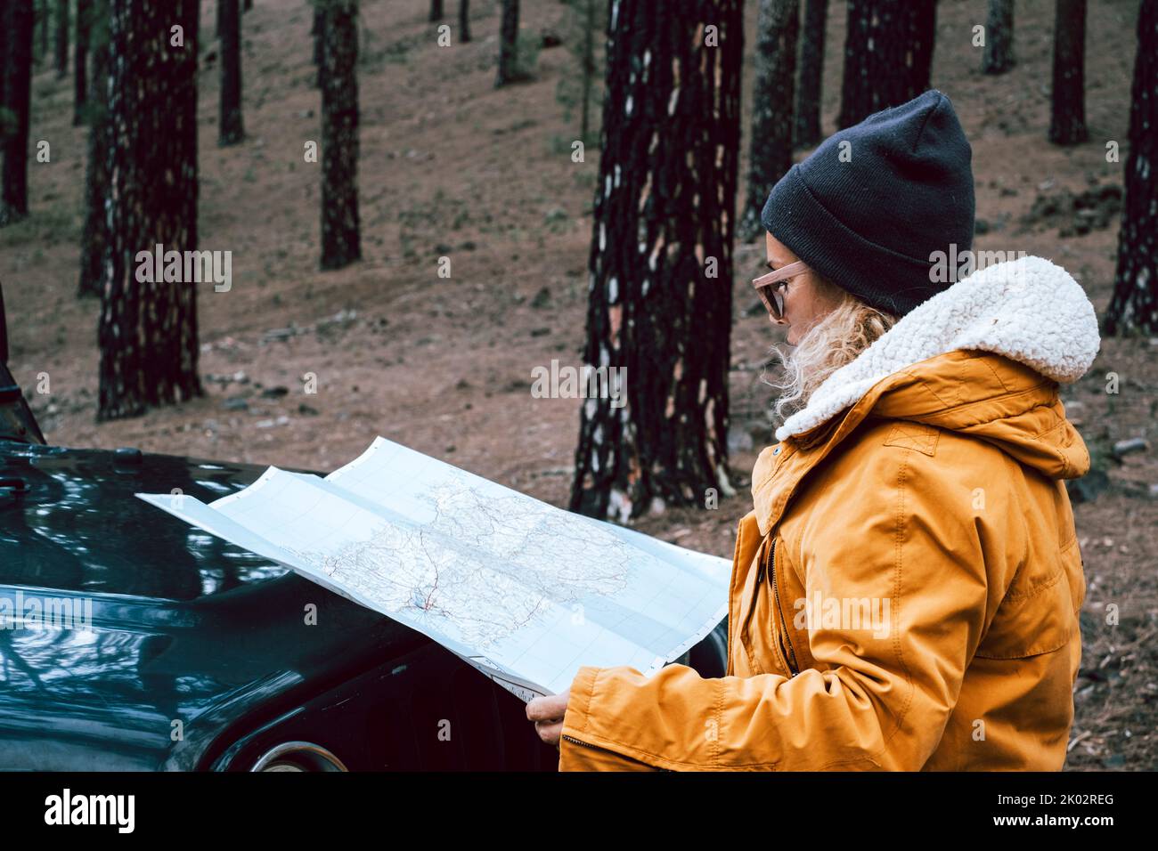 Woman check paper map in the woods forest on the front of the black off road car - concept of people and adventure lifestyle - travel wanderlust, life with independent female lost in the outdoors park Stock Photo