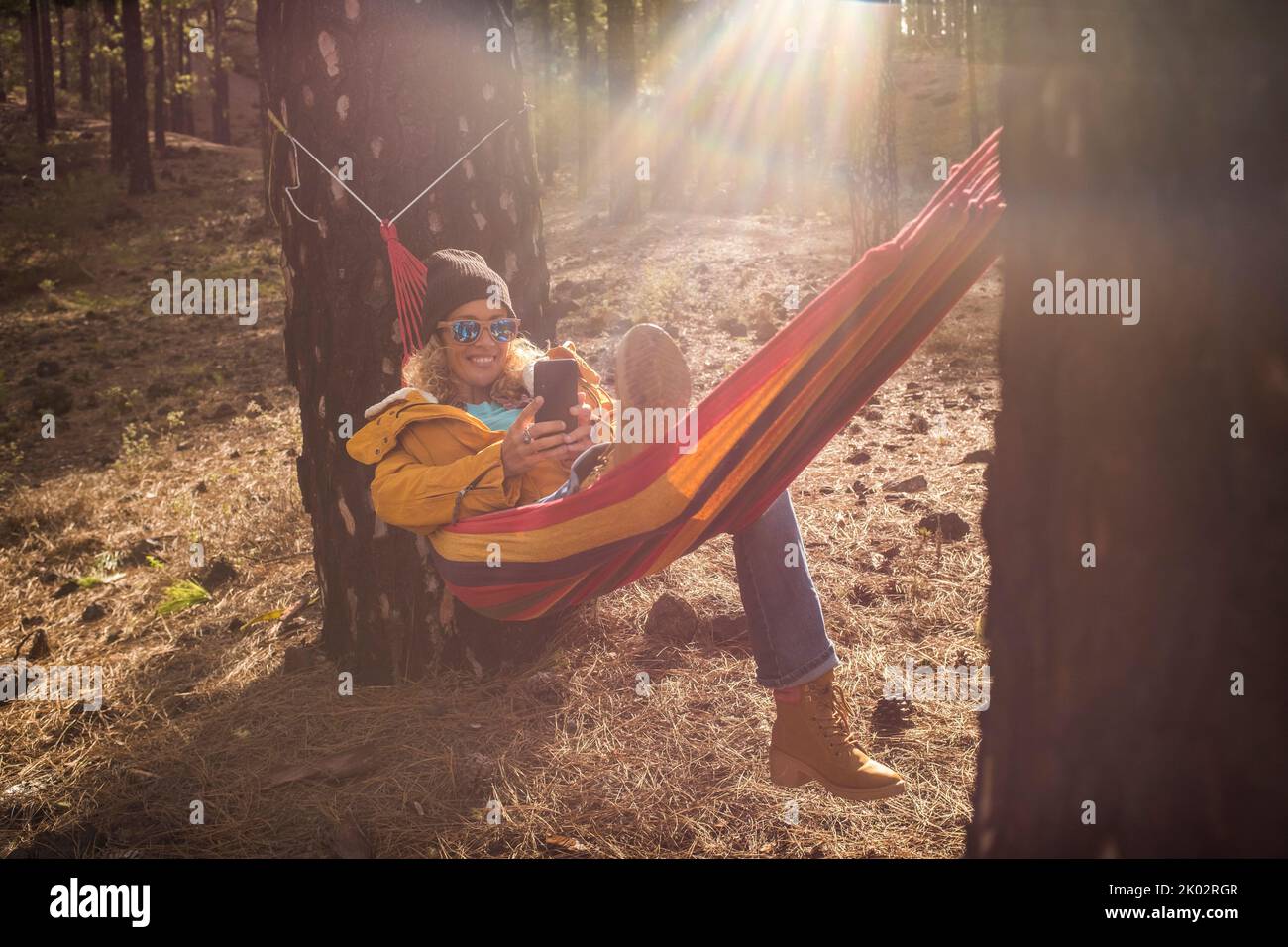 Cheerful portrait of beautiful woman enjoy relax at the mountain lay down on hammock on nature forest woods outdoors park and smiling to cellular phone - roaming connection and smart working job Stock Photo