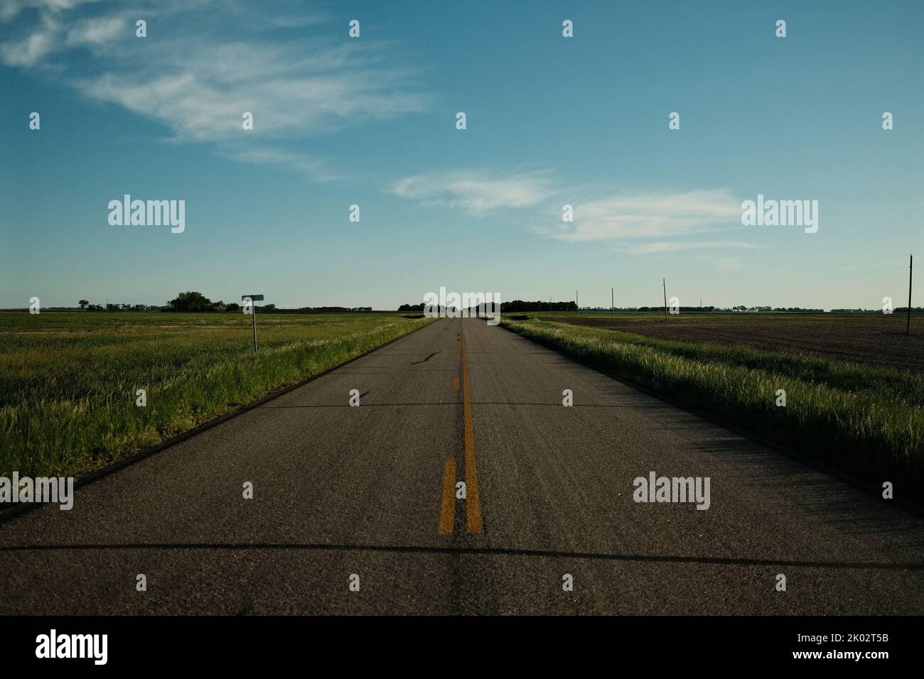 An asphalt road through fields under the blue sky Stock Photo - Alamy
