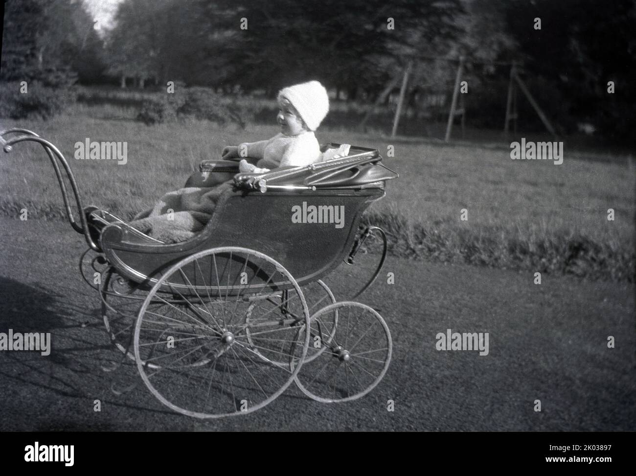 1929. historical, an infant girl sitting in a coach-built baby carriage or pram of the era, England, UK, with a wooden body and tyreless wheels. It is believed that the first baby carriage was invented in 1733 by English garden architect William Kent for the Duke of Devonshire as transport to amuse his children. it was a child's version of a horse-drawn carriage and became popular with the landed gentry of the day. Stock Photo