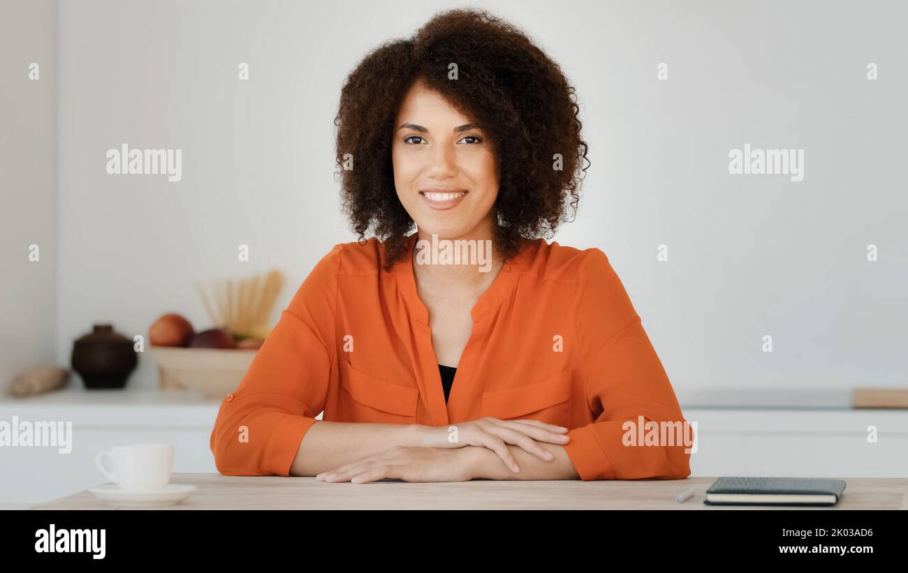 Webcam view smiling African American woman with curly hair sitting at home kitchen blogger female influencer vlogger waving hand hello greeting Stock Photo