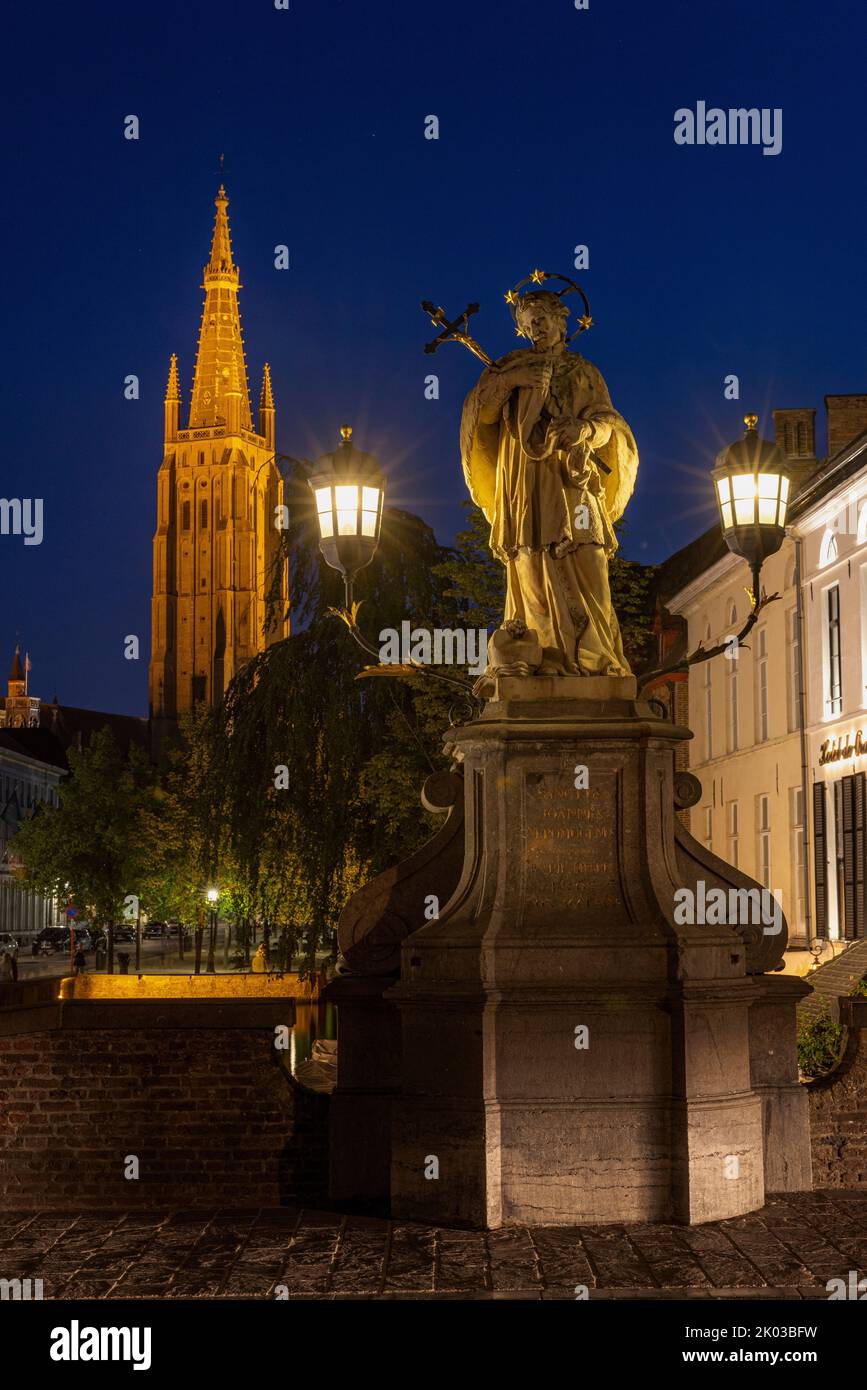Statue of St. John Nepomuk and tower of the Church of Our Lady at night. Bruges, Flanders, Belgium. Stock Photo