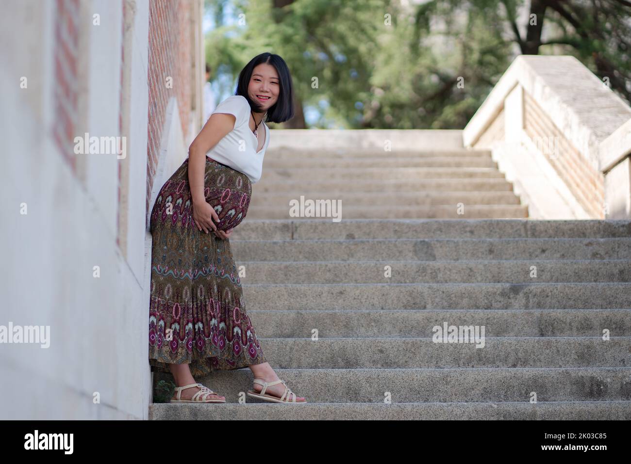 young happy and beautiful Asian Chinese woman posing outdoors happy and cheerful pregnant showing her belly proud smiling in pregnancy and maternity c Stock Photo