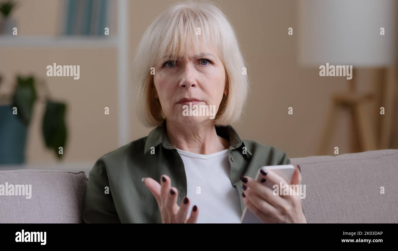 Upset Caucasian woman grandmother elderly lady with mobile phone feeling sad worry due to slow connection error online broken smartphone bad news Stock Photo