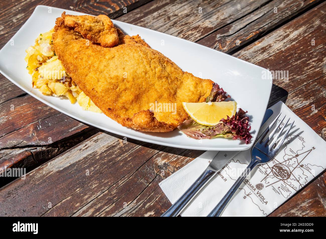 Ready-to-eat Wienerschnitzel with sauteed potato and garnish on white plate and rustic wooden table background Stock Photo