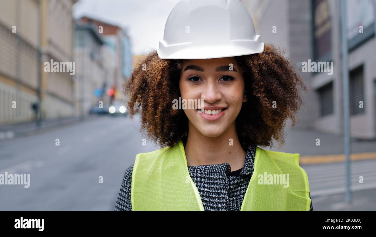 Female portrait worker profession close-up african american woman girl with curly hair civil engineer professional wearing safety helmet standing in Stock Photo