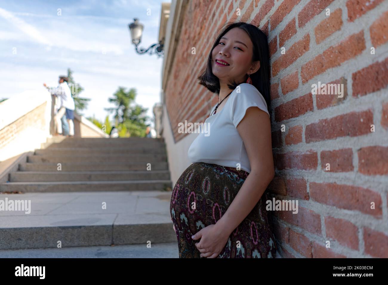 young happy and beautiful Asian Korean woman posing outdoors happy and cheerful pregnant showing her belly proud smiling in pregnancy and maternity co Stock Photo