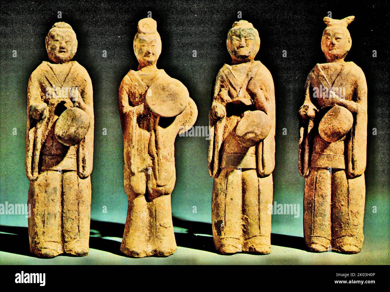 Northern Wei Dynasty figurines with dark soil, painted with white powder, wearing open-sleeved shorts with open collars reaching the chest, and wearing tight-fitting trousers with the toes slightly exposed. The first, third, and fourth figurines from the left each hold small drums. They all hold the handle of the drum in their left hand, and do not hold a stick in their right hand. The instrument held by the second figurine is a long-waisted drum. From the left, the first, second and third figurines wear headscarves, and the fourth figurines have their hair and heads tied together, and the hai Stock Photo