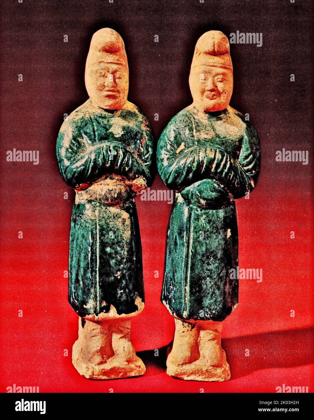 Tang Dynasty figurines with white, blue-glazed, standing on a small square platform, with their heads tied, and long blouses with round necks and narrow sleeves. Waist girdle, double forward gaze, serious and submissive expression. The figurines are covered with blue glaze. The head, crown, and feet are all unglazed, and the production is relatively simple. The two figurines have the same demeanour and clothing. Stock Photo