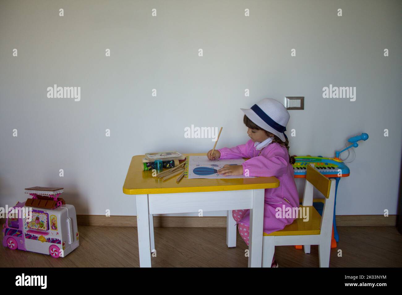 Adorable little girl with pink hat and apron playing with pencil colors in a notebook. Back to school and first day of kindergarten Stock Photo