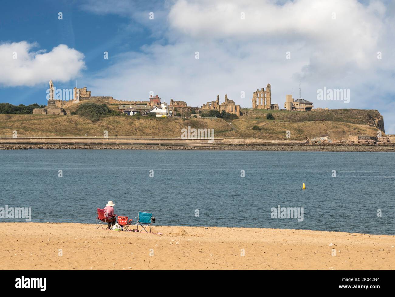 A person sits on Littlehaven Beach, South Shields, looking across the river Tyne to Tynemouth Priory and Castle, England, UK Stock Photo